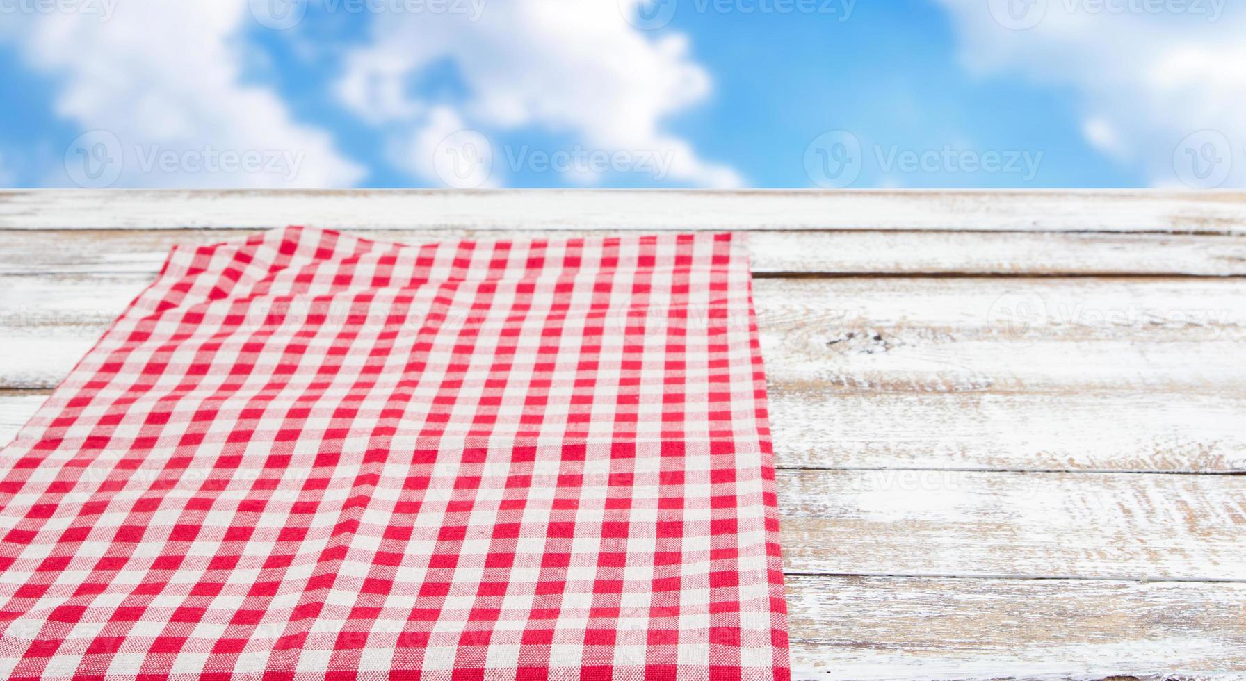 Mantel rojo sobre la mesa de madera vacía, fondo de cielo borroso foto