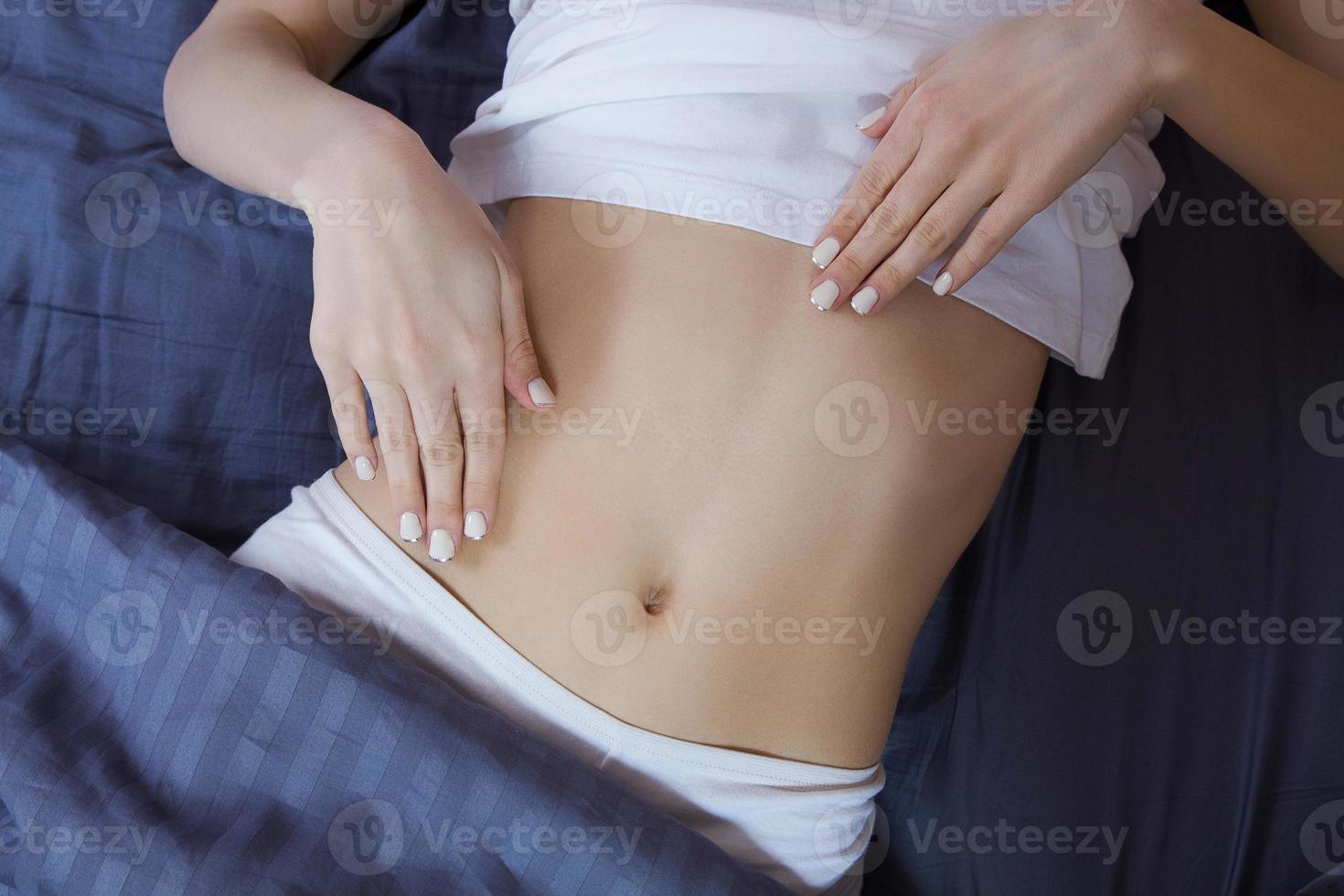 Healthy nutrition and belly health concept. Close up of woman flat stomach. Girl in bed with hungry feeling. Top view photo