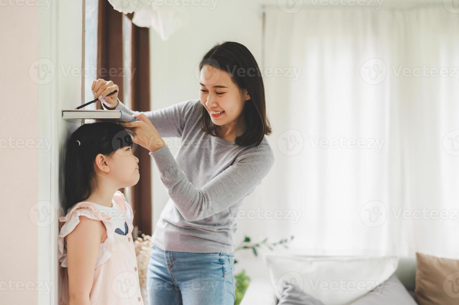 Mother measuring height of little girl near wall photo