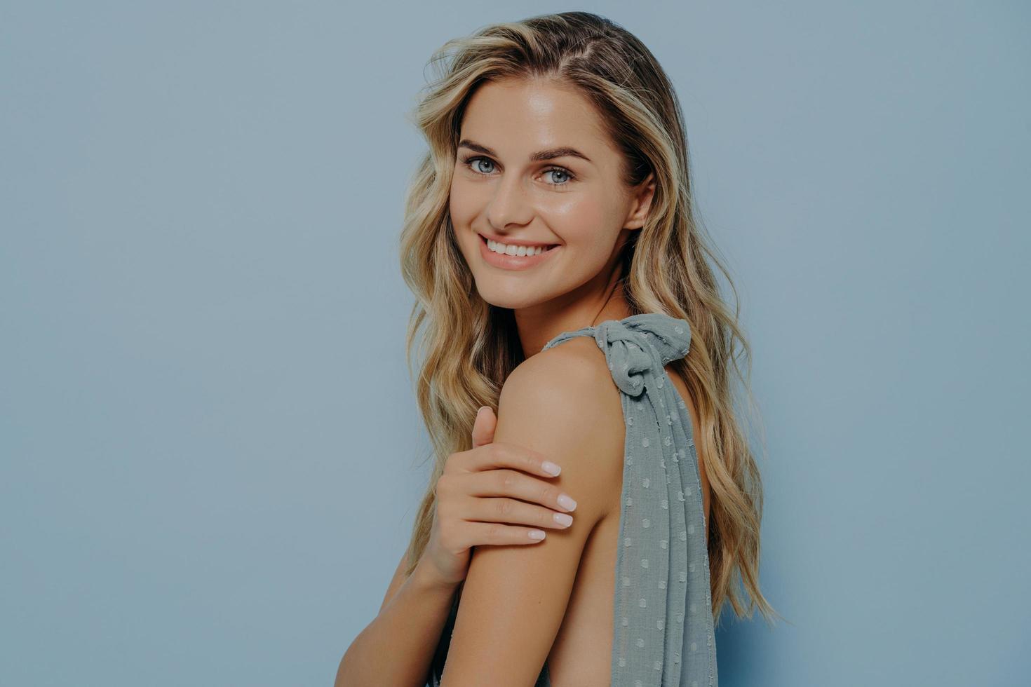 Young beautiful female in elegant dress smiling tenderly while looking at camera over her shoulder photo