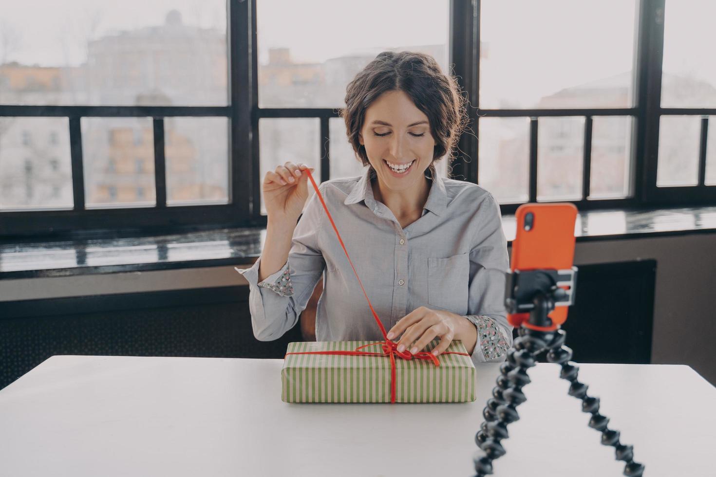 emocionada bloguera hispana abriendo una caja de regalo grabando un video sobre el regalo de Navidad para su blog foto