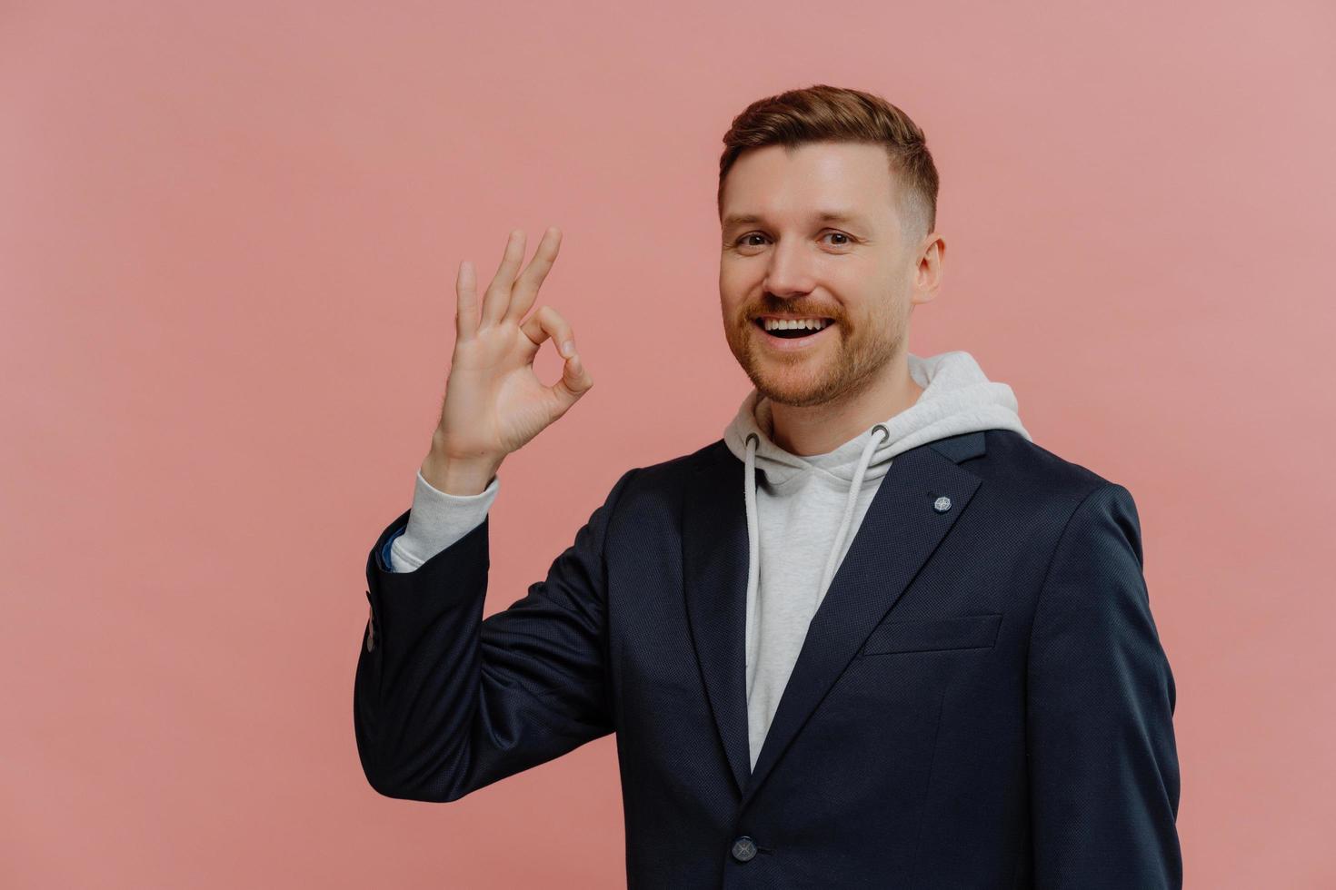 hombre pelirrojo feliz que muestra un gesto bien aislado sobre una pared rosa foto