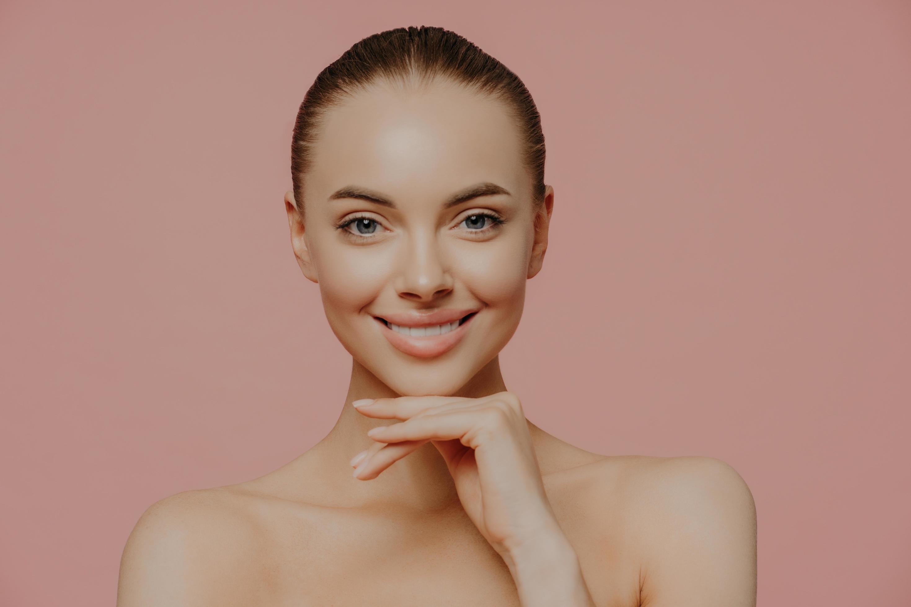 Pretty young European woman touches chin gently, enjoys flawless of
