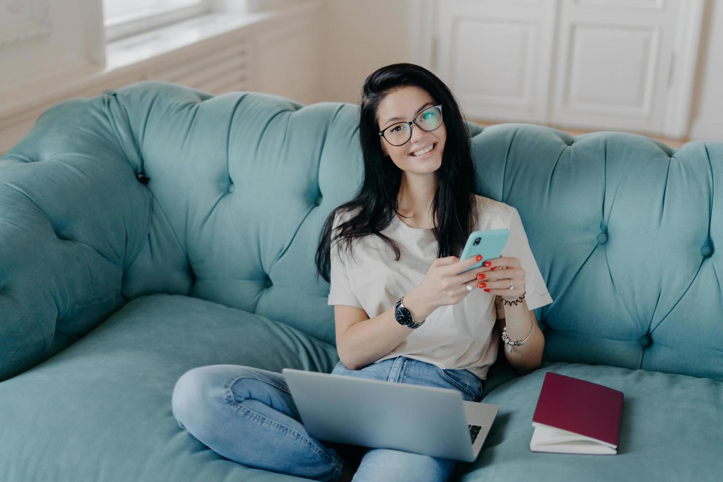 vista superior de una hermosa morena con gafas transparentes y ropa informal, envía archivos, navega por las redes sociales, posa en un cómodo sofá, revisa las noticias, trabaja de forma remota en el área de publicidad foto