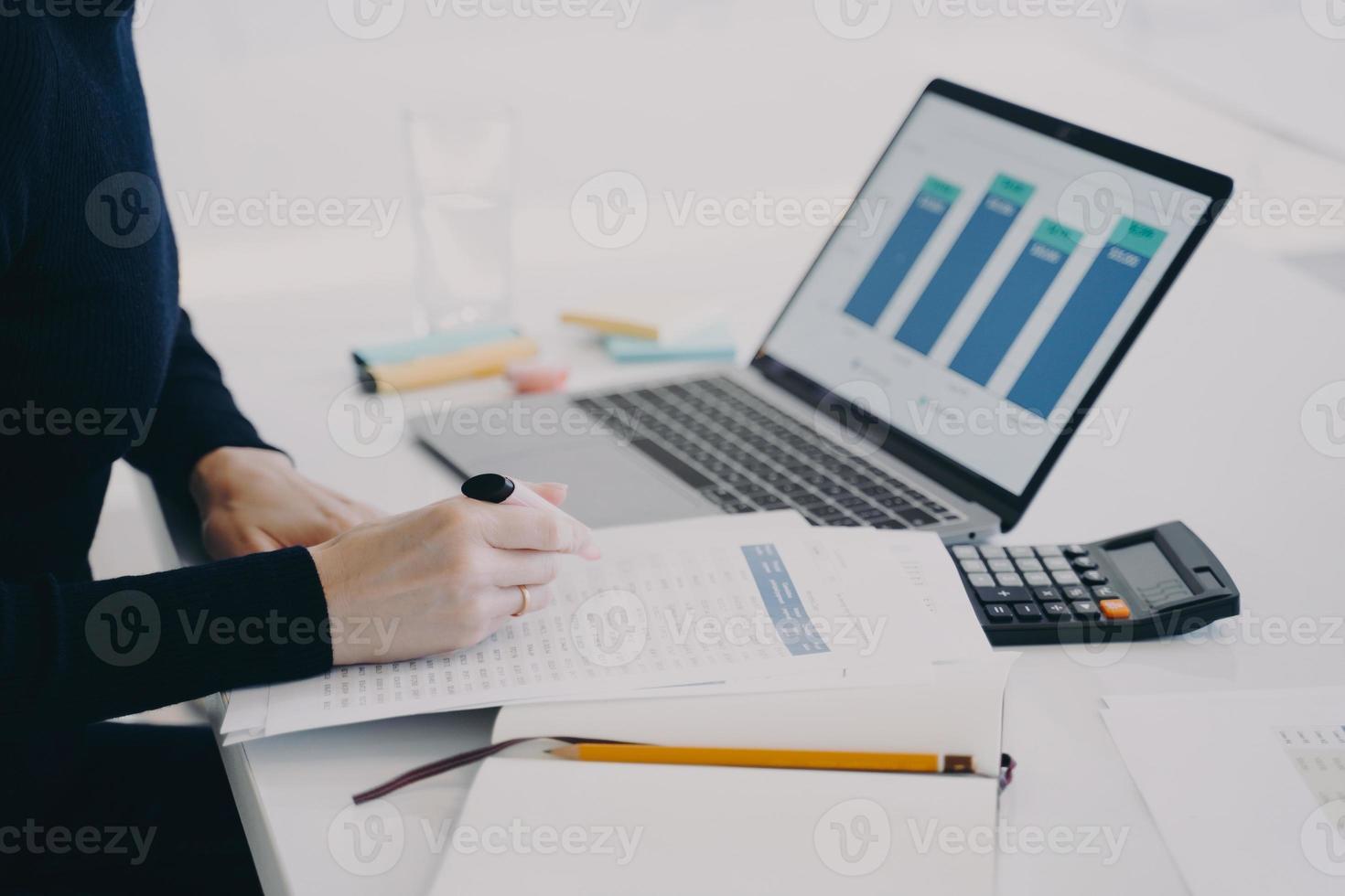 Hands of european woman at the desk in office. Entrepreneur is working at laptop and calculating. photo