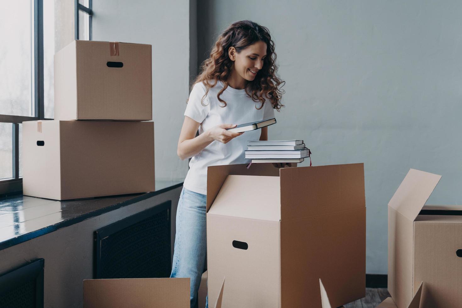 Young woman, student is housing in residential room. European woman unpacking boxes with books. photo