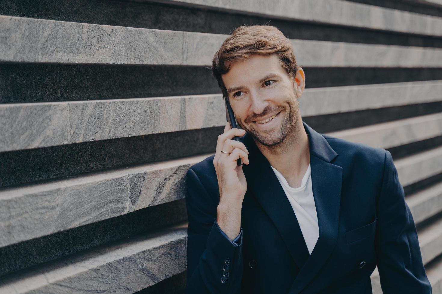 Handsome smiling man in stylish speaking on smartphone outside, enjoying conversation photo