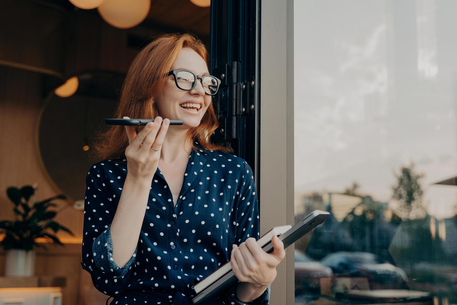 Woman with red hair holds phone talks on speakerphone with friend makes voice recognition photo