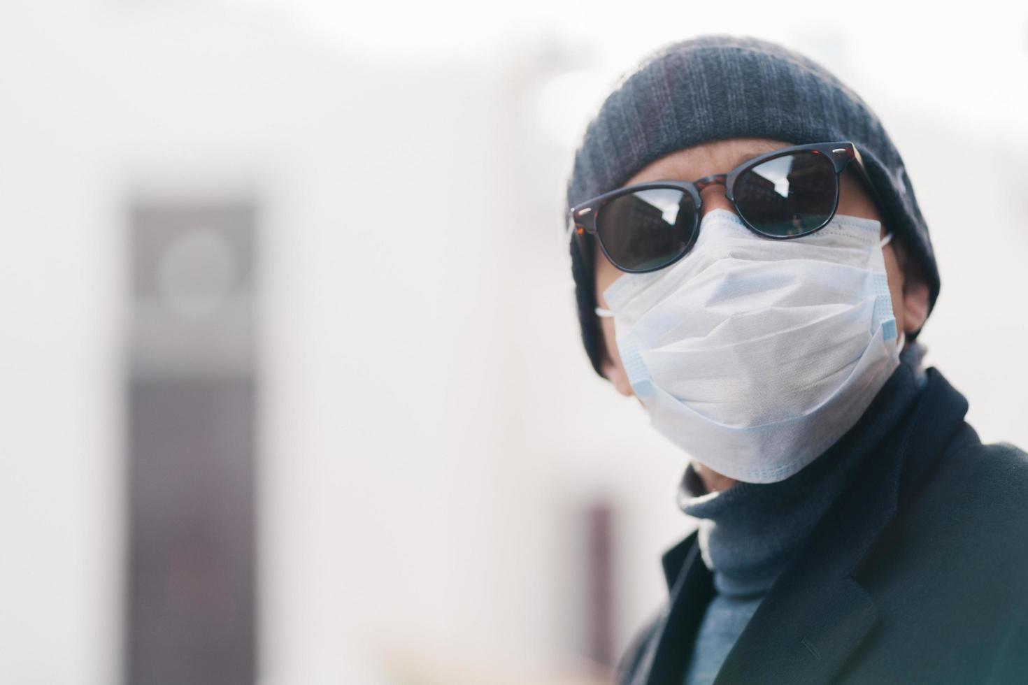 Close up shot of man wears hat and disposable medical mask, afraids of getting infected with coronavirus, poses against blurred background, copy space for your promotional content. Covid-19. photo