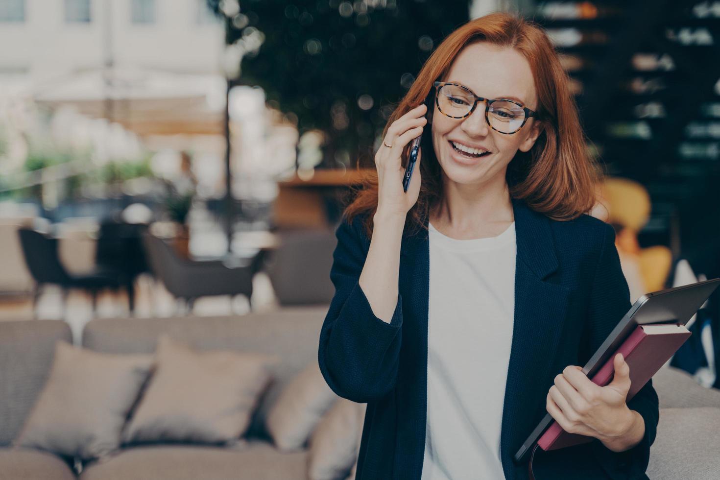 Happy smiling red haired business woman in optical eyewear enjoying telephone conversation photo