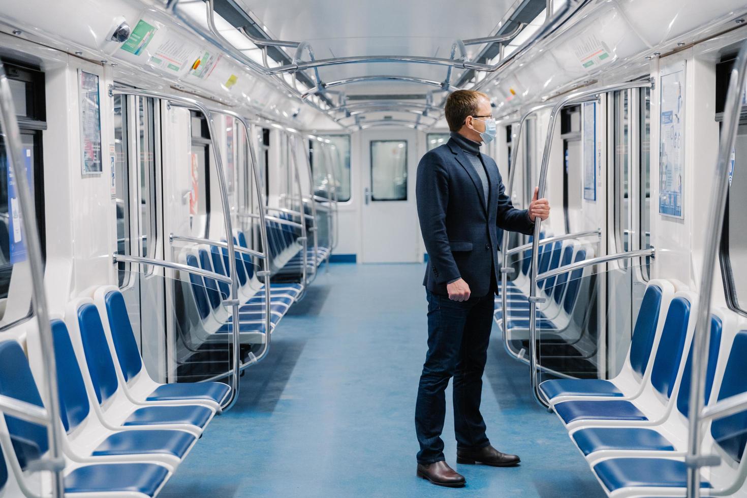 Shot of man who doesnt work at distance during quarantine, wears face mask to avoid coronavirus infection, poses in empty underground carriage with no people. Health awareness for pandemic protection photo