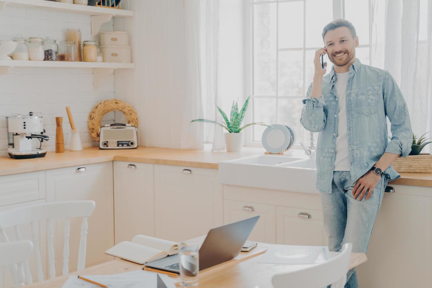 hombre feliz freelancer involucrado en una agradable conversación telefónica en la cocina foto