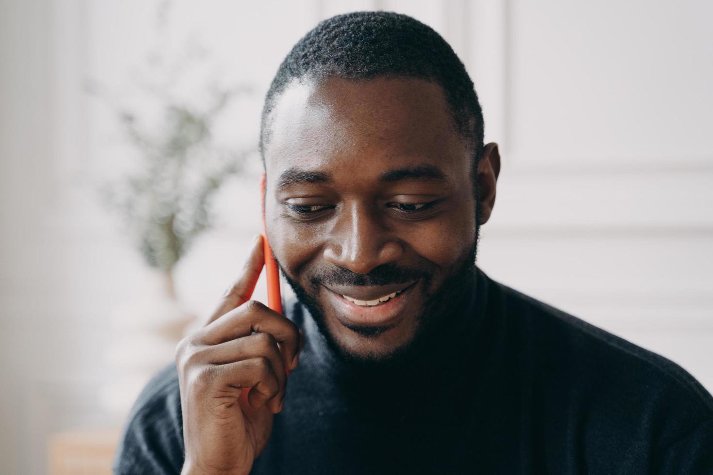 Cheerful young African American businessman talking on smartphone while working distantly at home photo