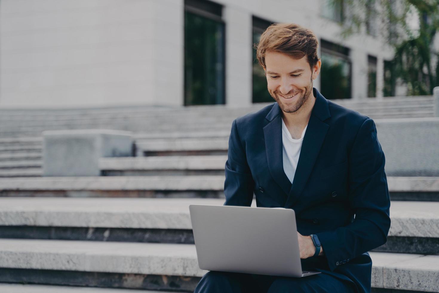 Young businessman sits on steps uses laptop organizes meeting online with investors photo