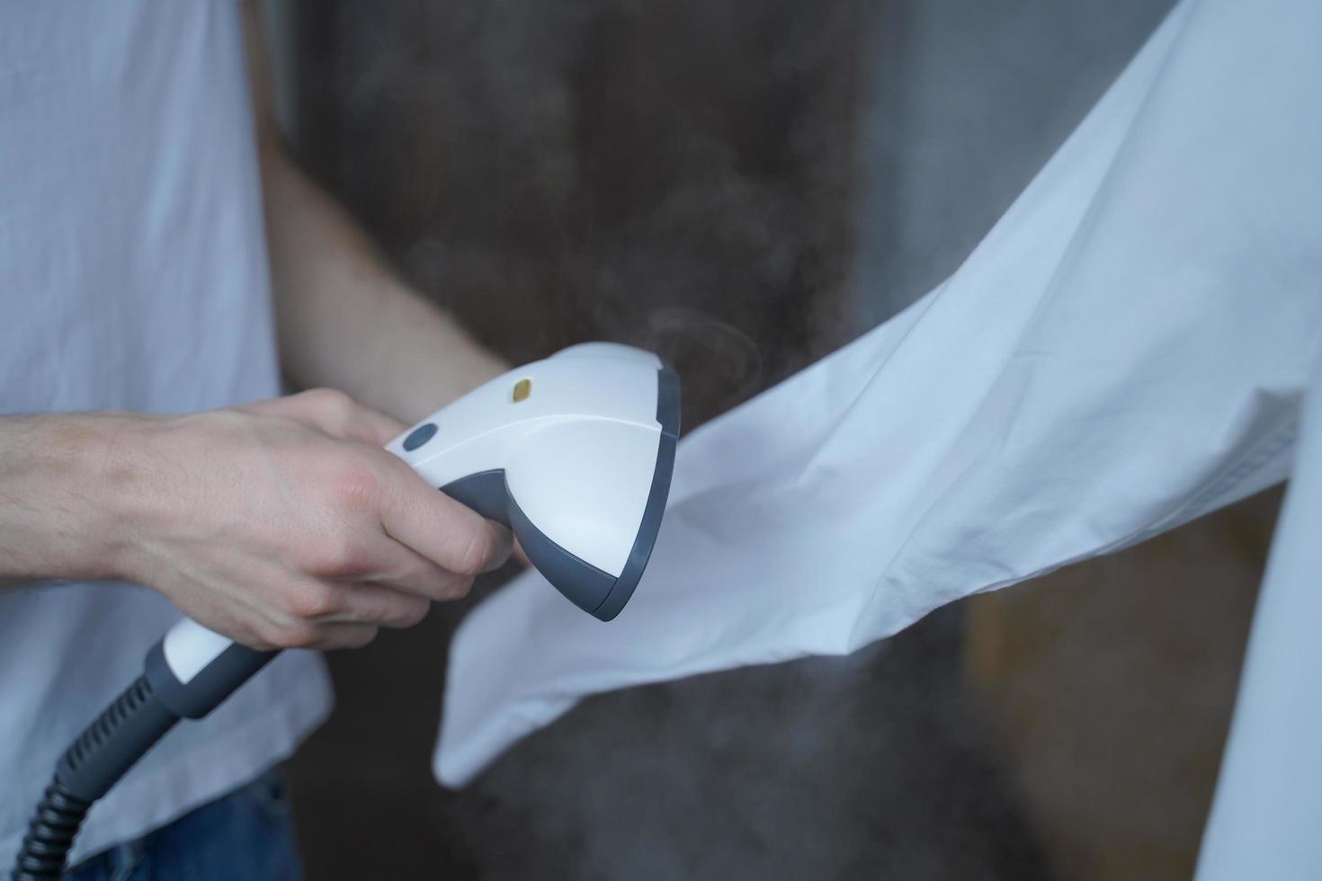 Cropped photo of man using steamer neatly ironing white shirt while holding long sleeve