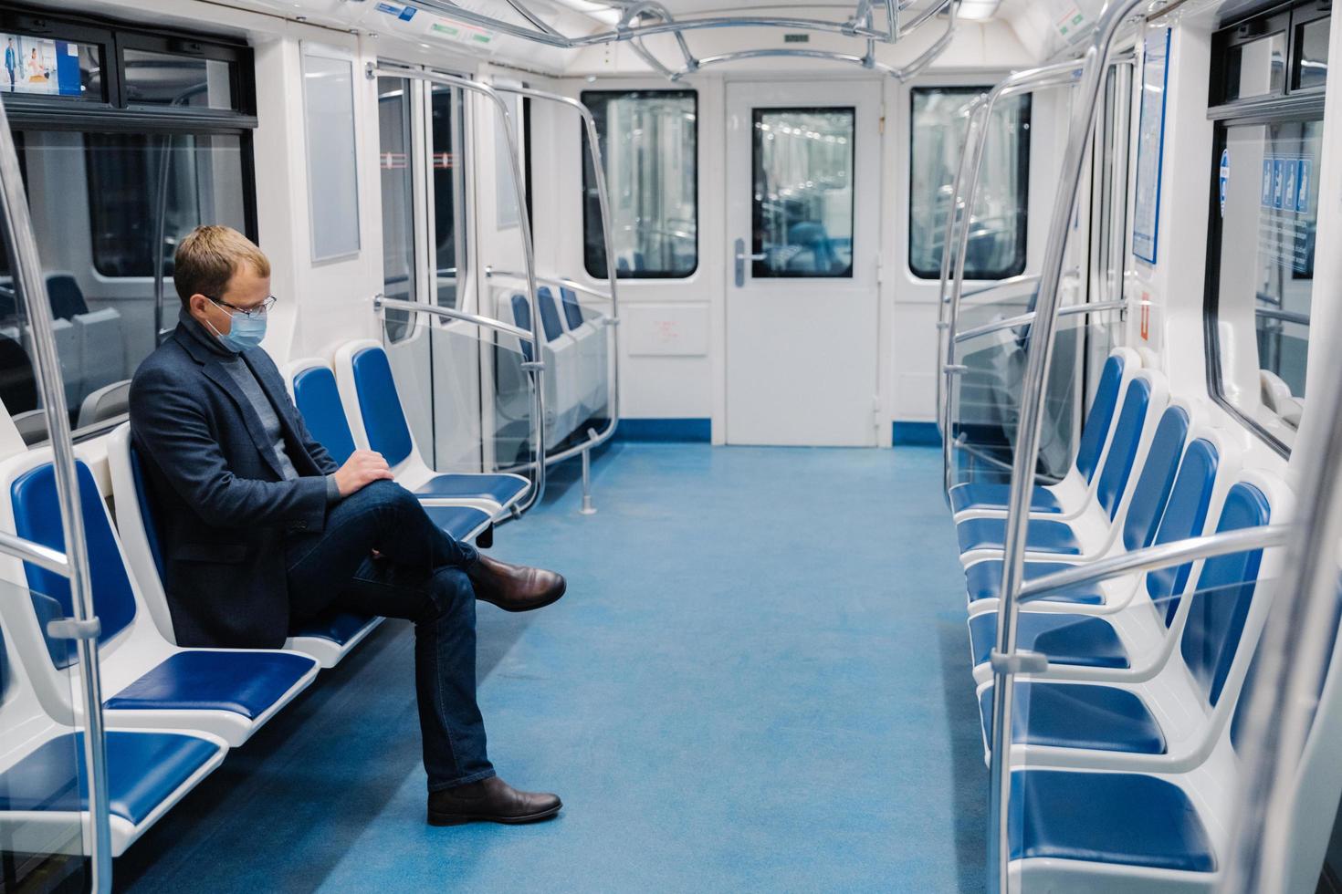 Man uses medical face mask, sits alone in metro carriage, commutes to work by public transport, avoids covid-19, uses equipment for staying safe during coronavirus pandemic. Health care concept photo