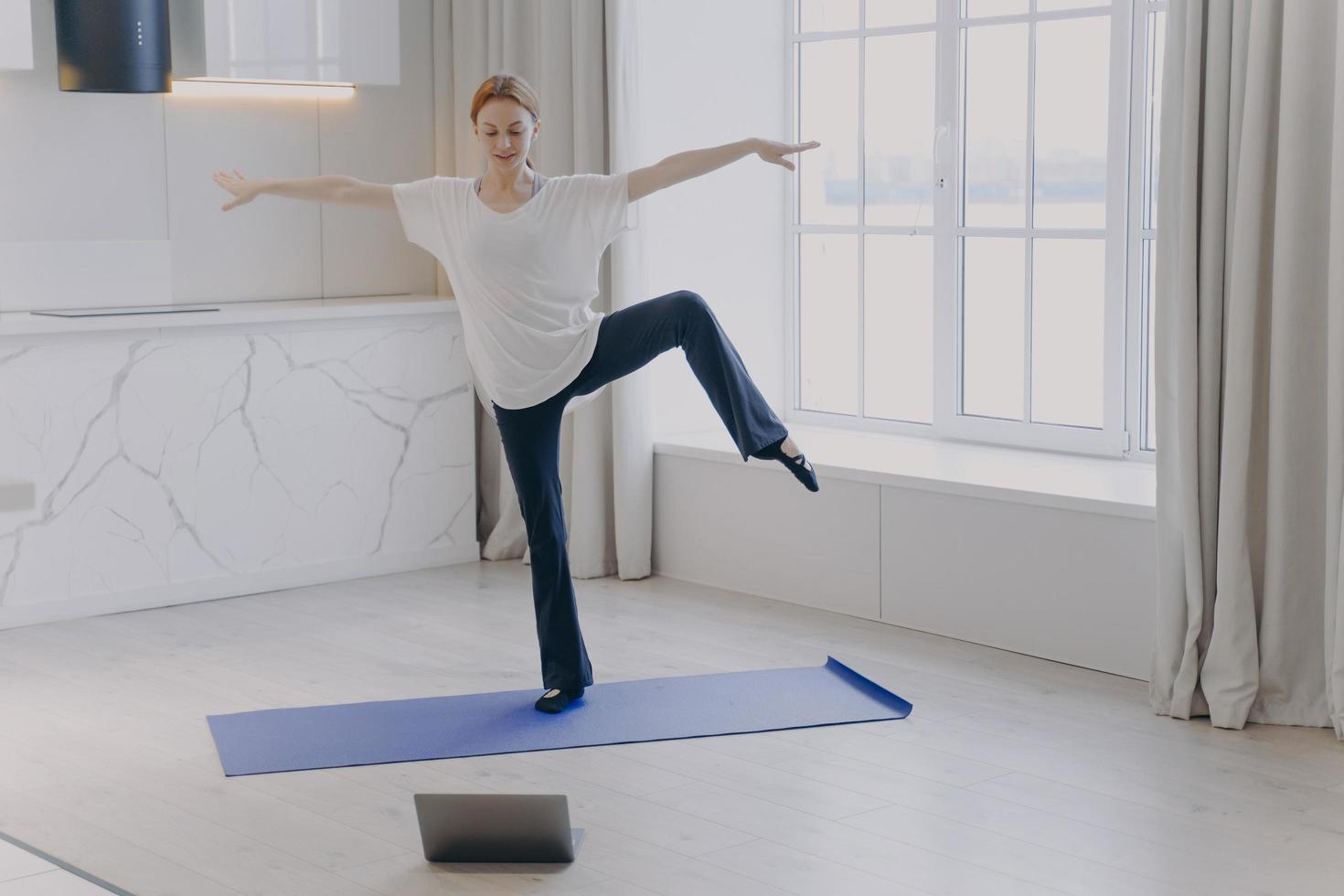 Woman is doing balance exercise having sports in front of camera. Home classes on quarantine. photo