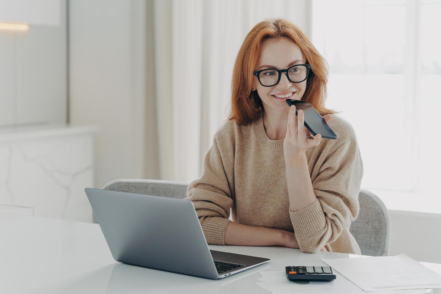 Smiling woman accountant financier uses voice recognition system on smartphone, records audio message photo