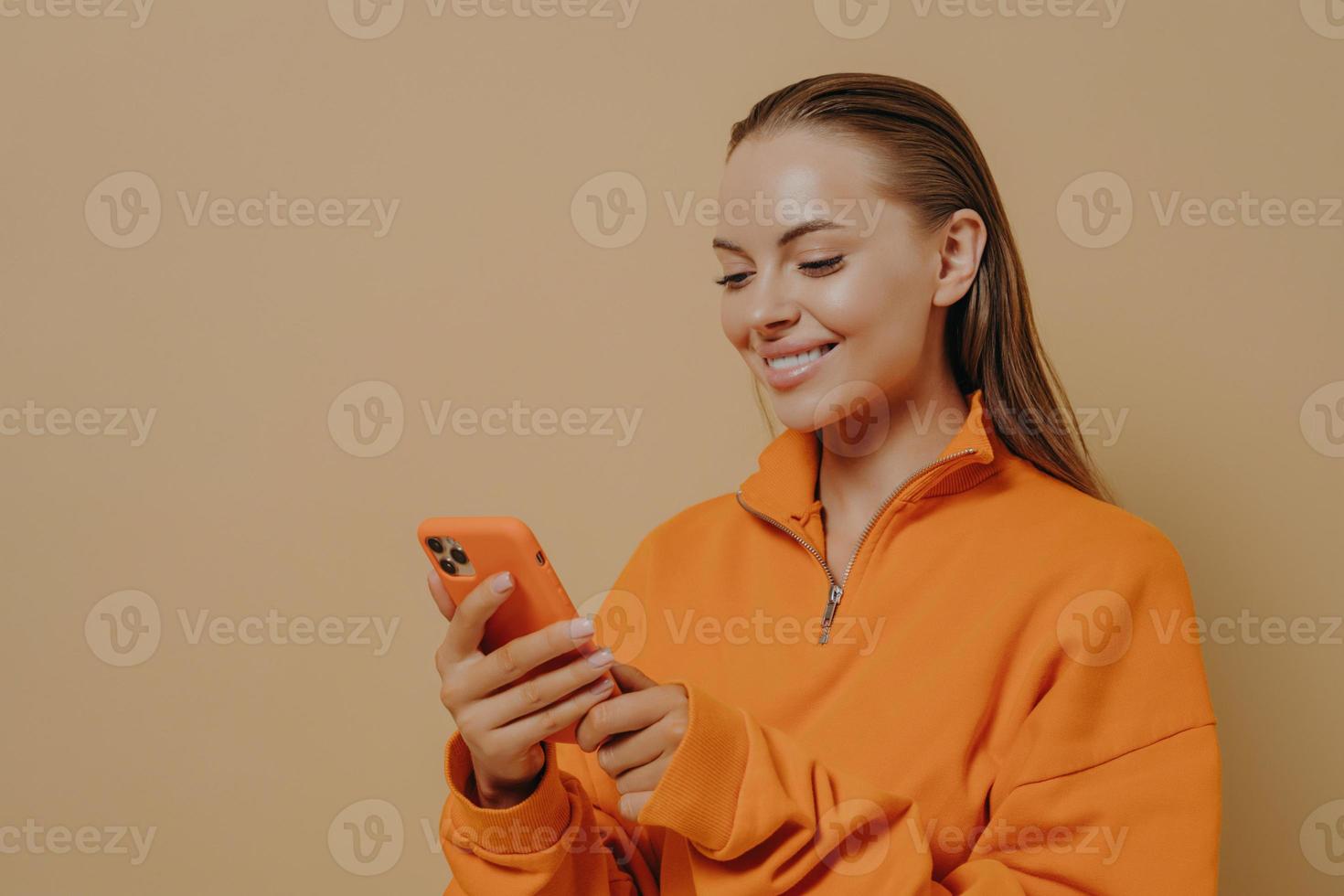 feliz y encantadora mujer joven sosteniendo un teléfono inteligente en las manos y sonriendo, charlando en las redes sociales foto