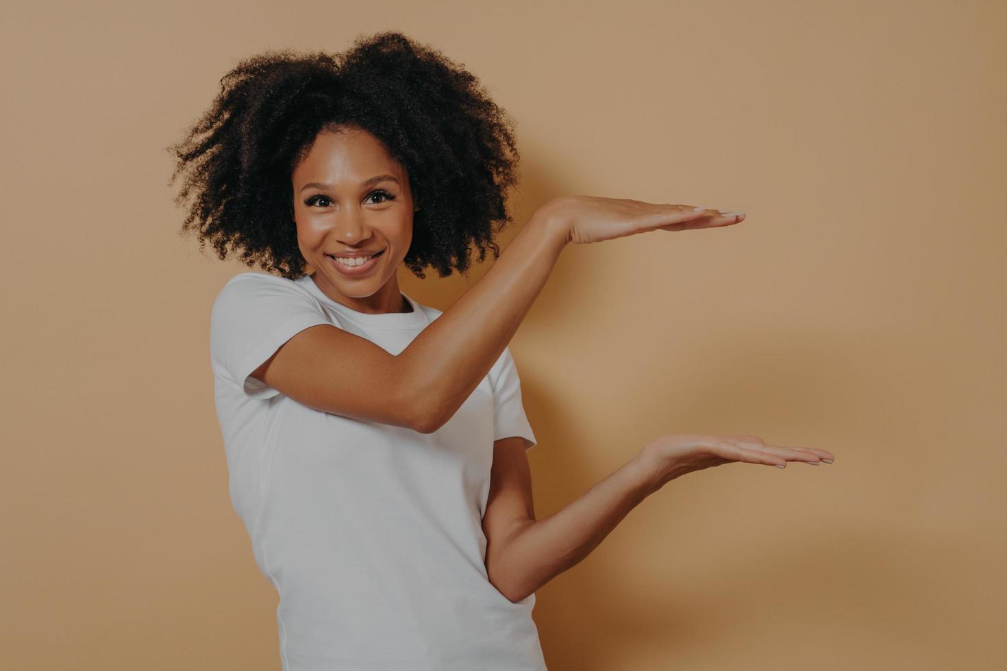 Young dark skinned showing large object, shaping box with both hands, isolated over beige background photo