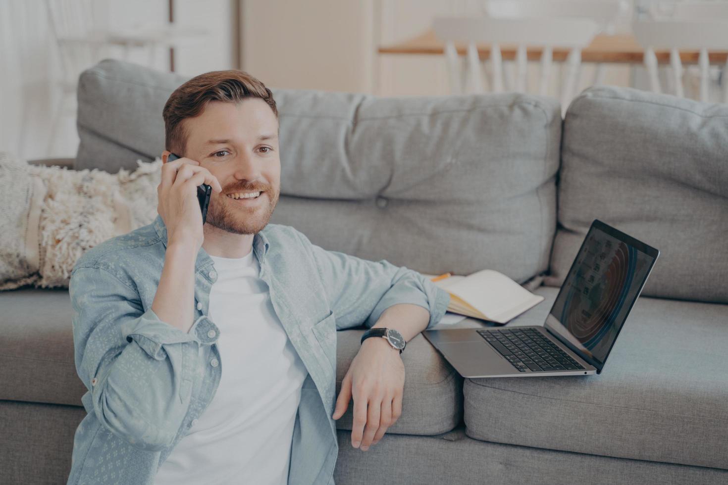 Young male company employee working remotely from home calling boss to tell good news photo