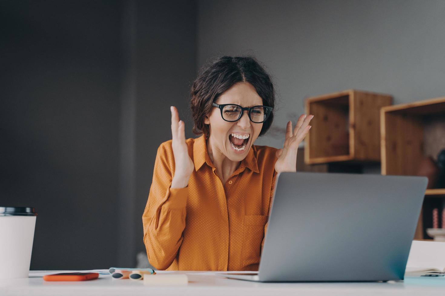 mujer de negocios italiana loca gritando angustiada por la desesperanza mientras trabaja en línea en una laptop foto