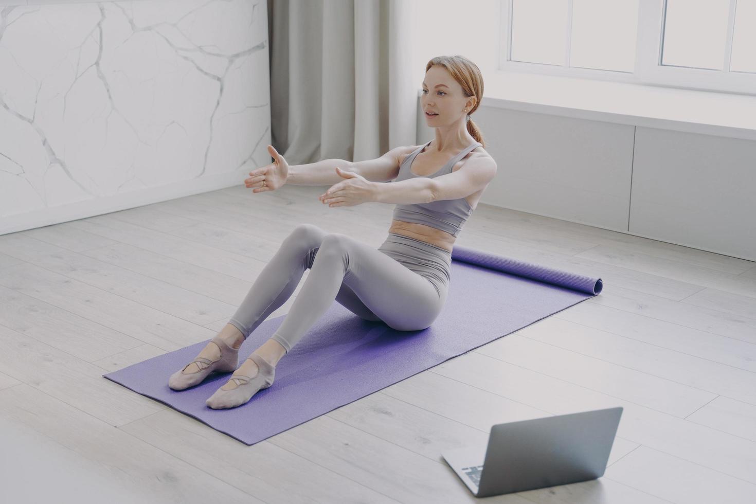 Press exercise and pilates at home. Video lessons on laptop. Concept of distance fitness classes. photo