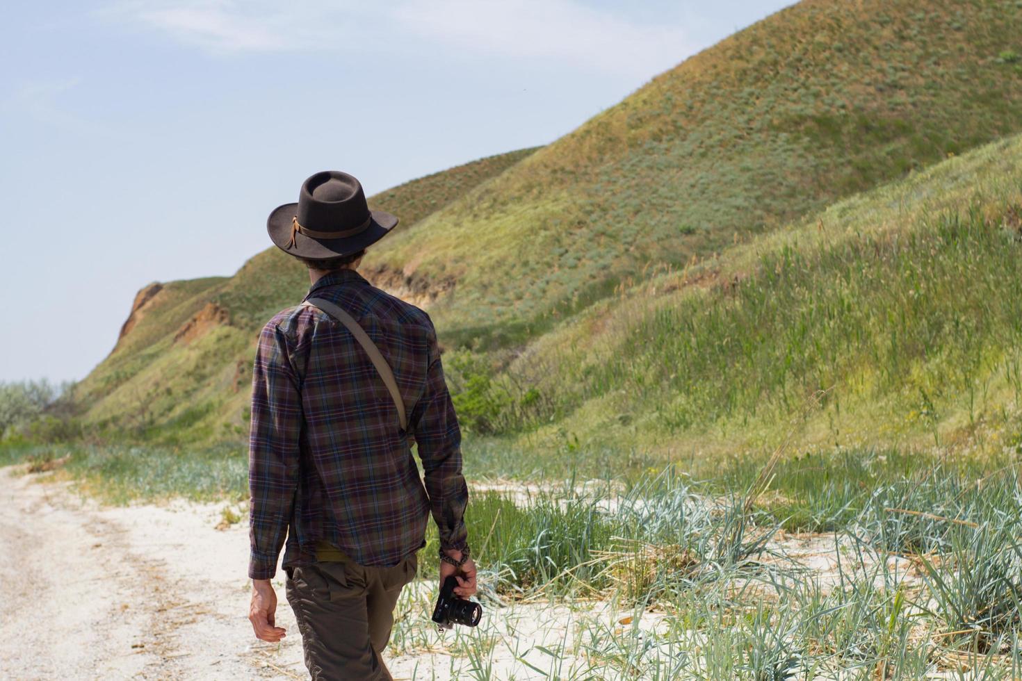Back view of young male hiker in cowboy hat walking outdoors in summer day. Hipster traveler. photo