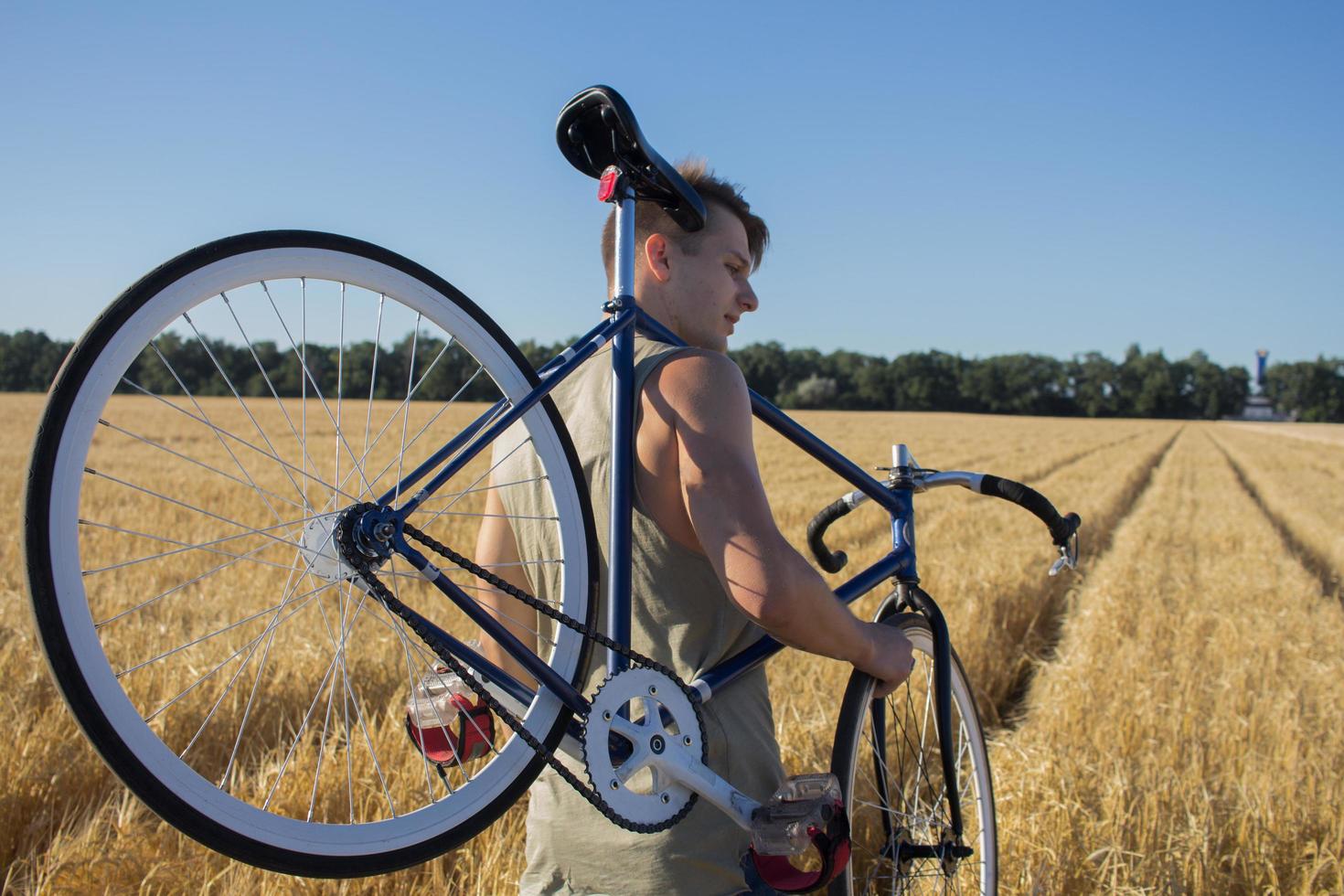 Young man ride fixed gear bike on the country road, fields and blue sky background photo