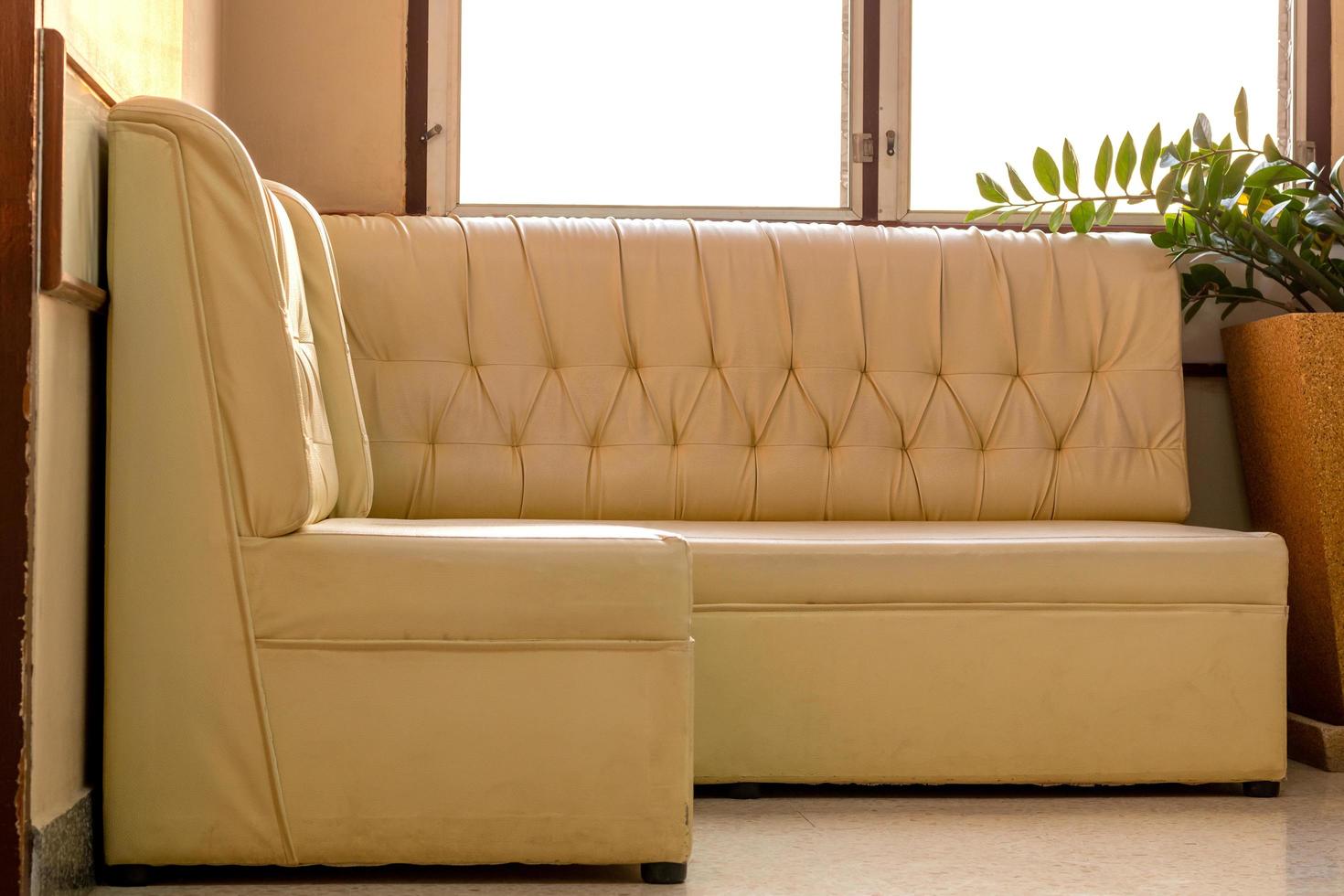 Old cream-colored sofa in the corner of the room with window light. photo