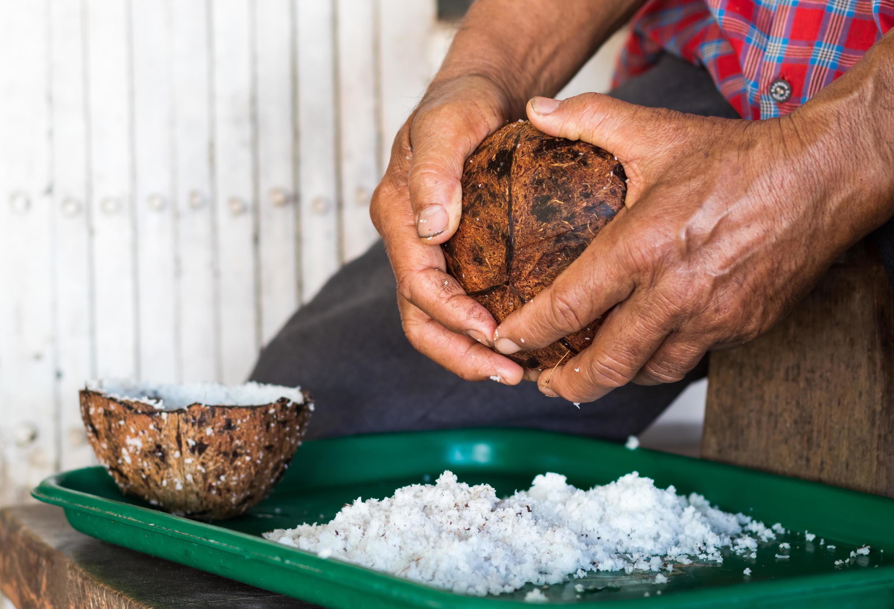 anciano con los dedos para raspar el coco en la bandeja. 7664904 Foto