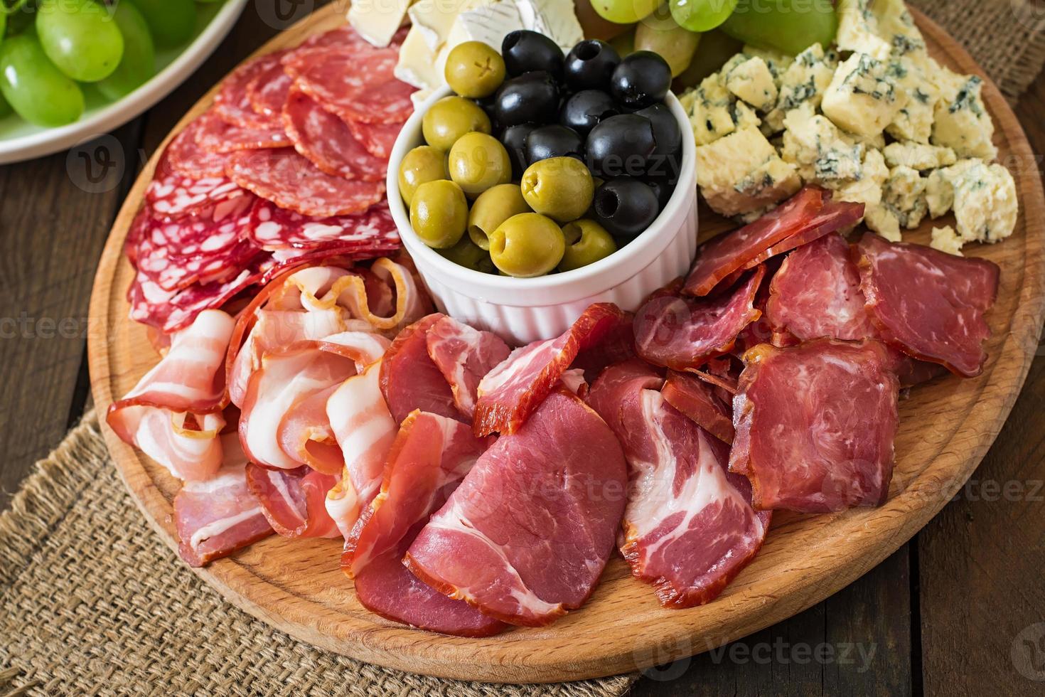 Antipasto catering platter with bacon, jerky, salami, cheese and grapes on a wooden background photo