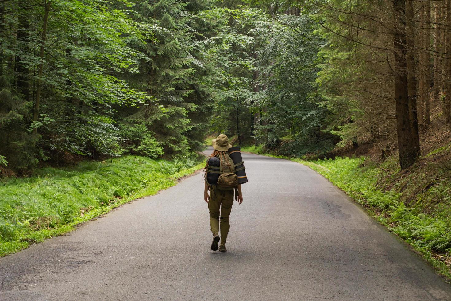 young woman hiker walking on narrow road through summer green forest photo