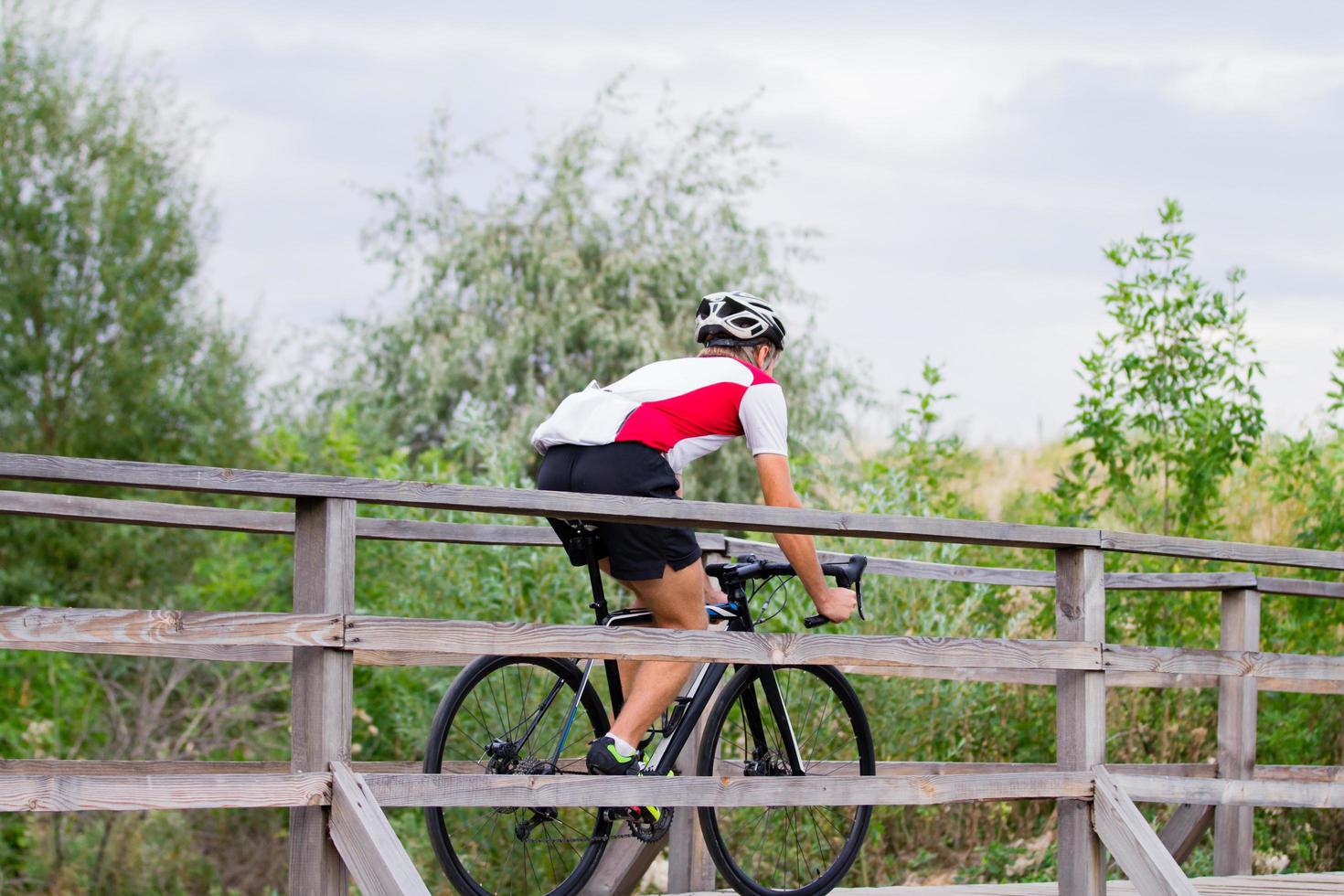 ciclista profesional en uniforme y casco en el viejo puente de madera, fondo del campo foto