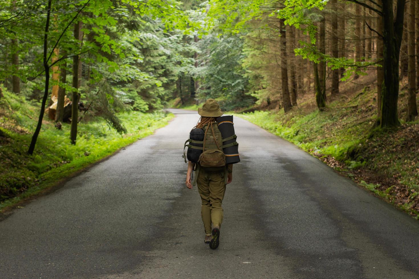 young woman hiker walking on narrow road through summer green forest photo