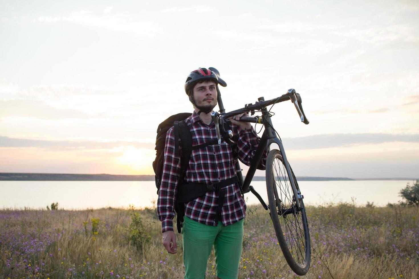 silueta de un hombre con bicicleta de carretera de gira mirando y haciendo una foto de la puesta de sol en el lago en el teléfono celular