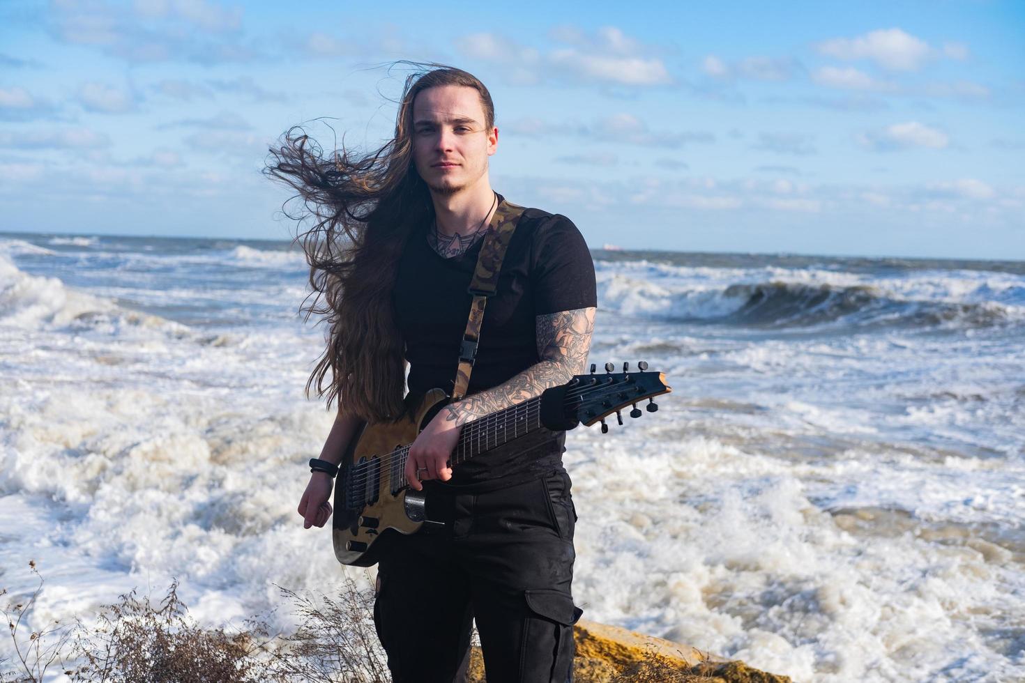 Young male in black and long hair play on guitar on the beach photo