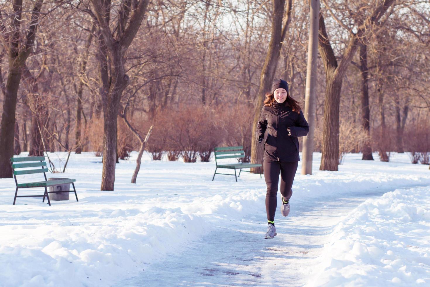 young woman athlete in black sport suit run in winter park photo