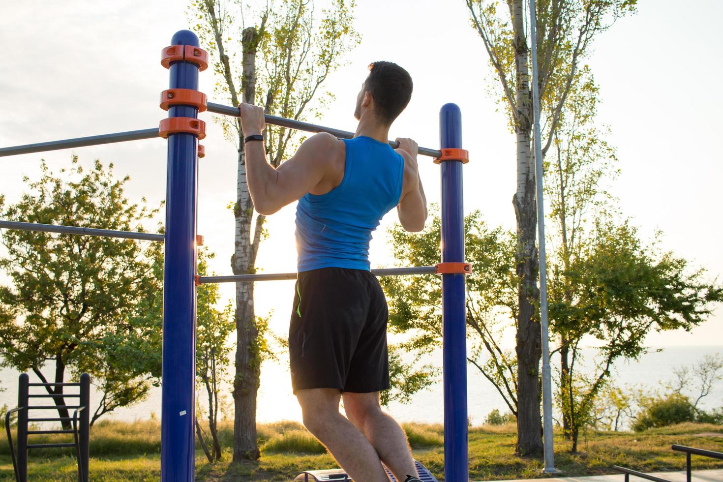 Muscular man doing pull-ups on horizontal bar, training of strongman on outdoor park gym in the morning. photo