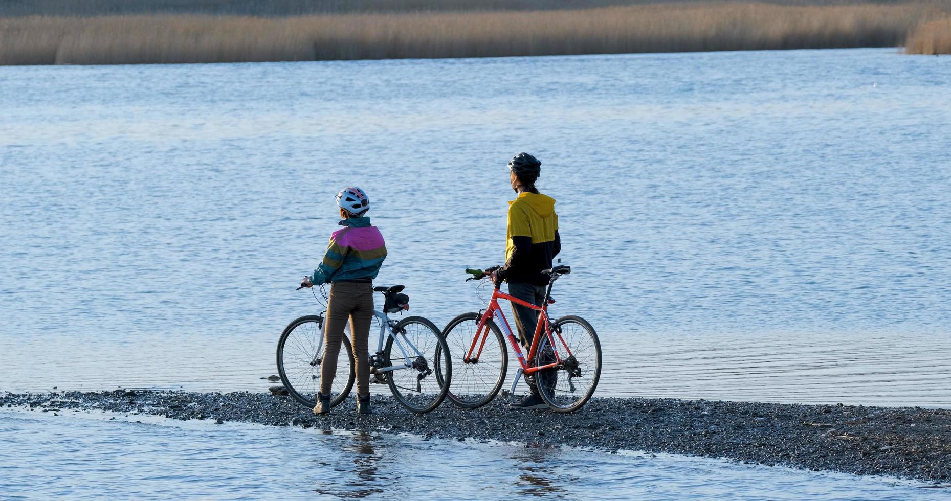 Couple of male and female ride on bicycles near river during sunset photo