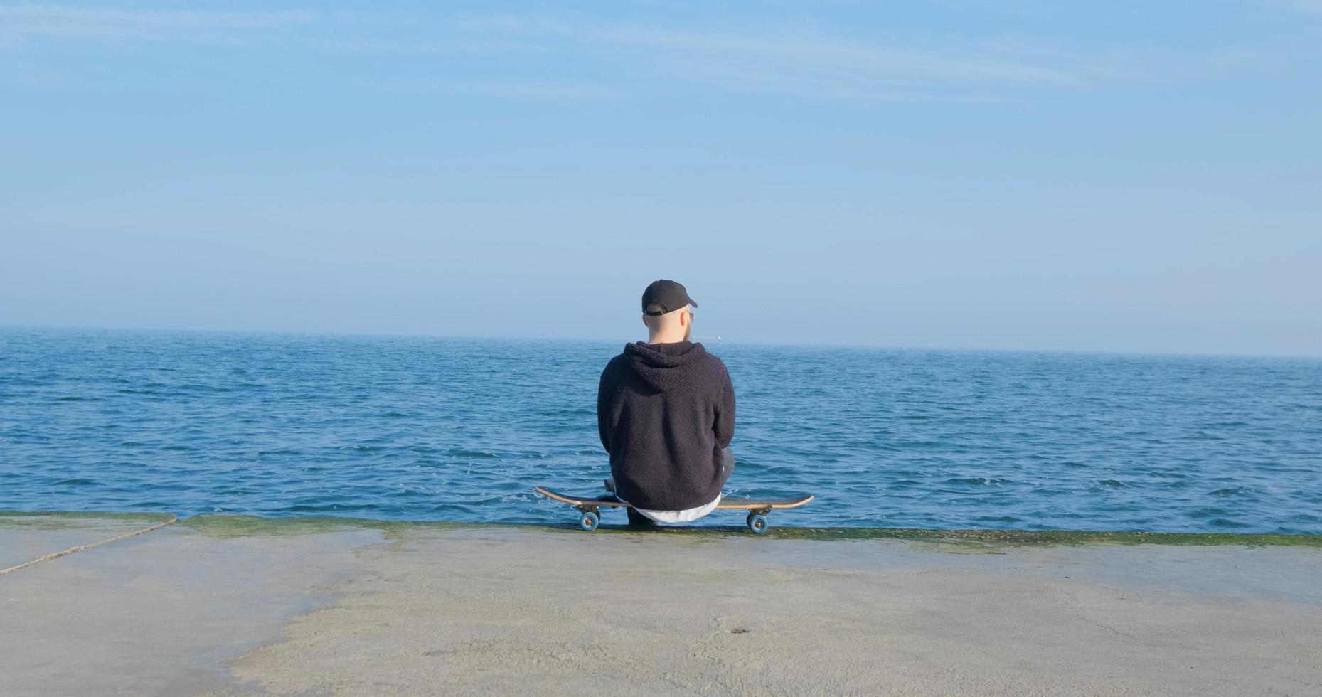 macho joven con monopatín relajándose cerca del mar foto