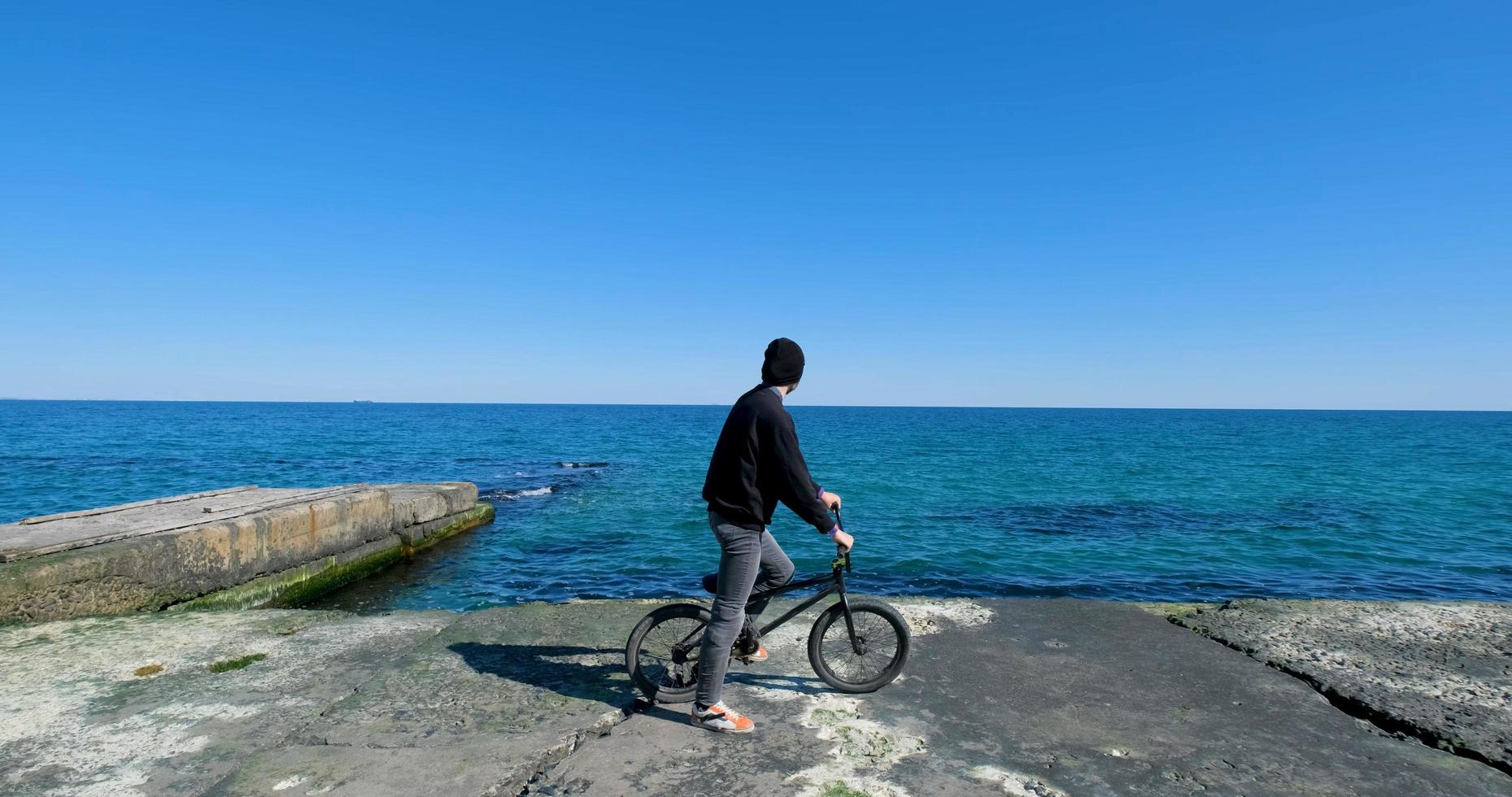 macho joven con monopatín relajándose cerca del mar foto