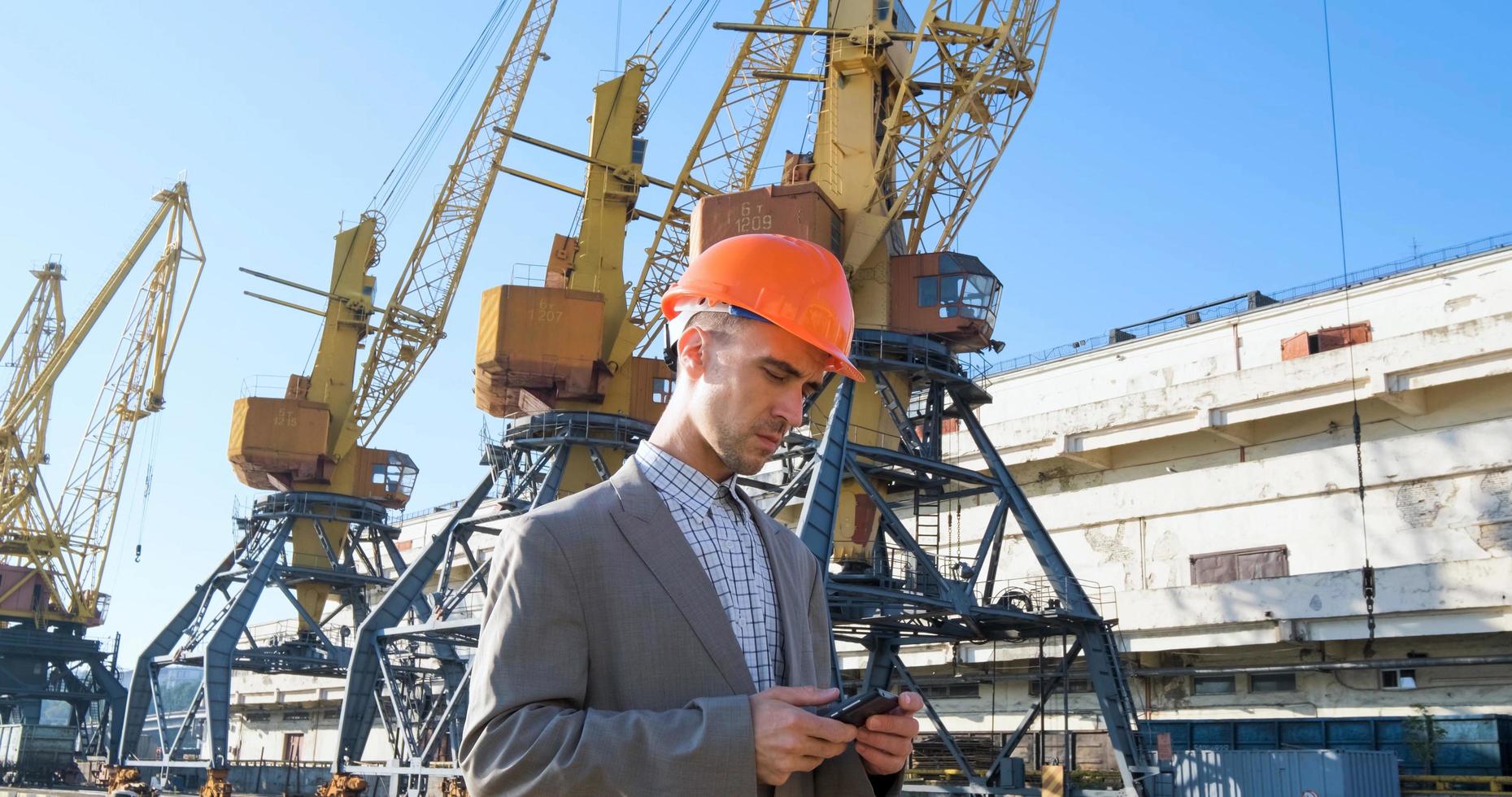 Young male worker of sea harbor in helmet, cargo manager in suit and halmet works outdoor , cranes and sea background photo