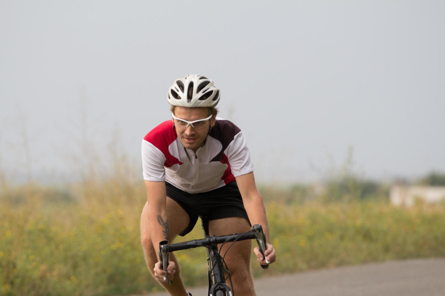 Bicycle racer in helmet and sportswear training alone on empty country road, fields and trees background photo