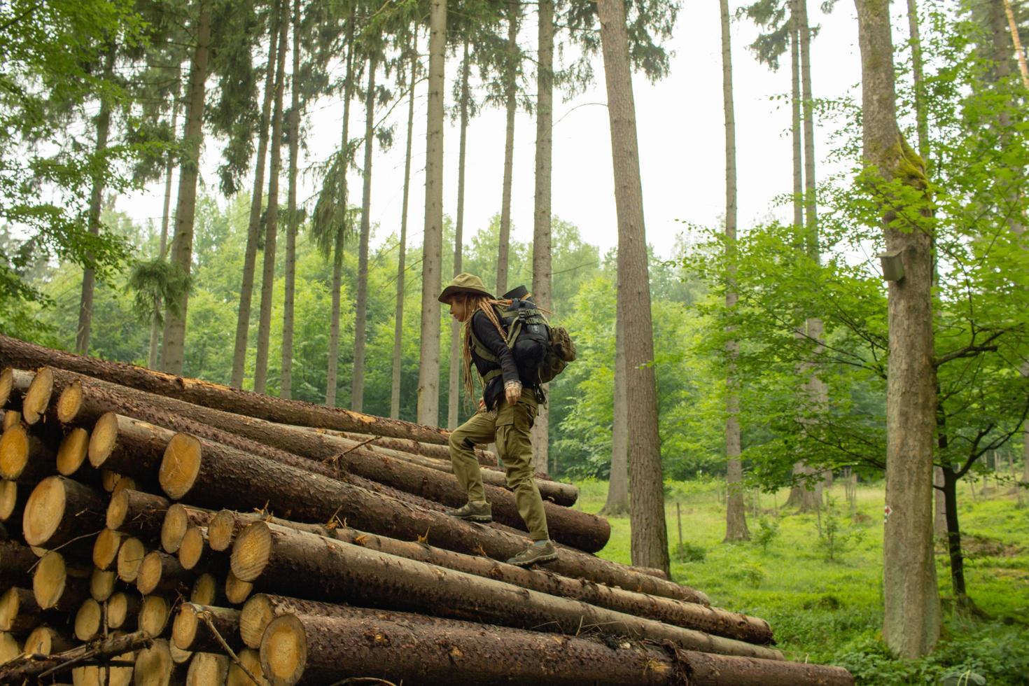 joven excursionista posando cerca de la harina de aserrín en el bosque de pinos. muchos troncos de árboles en el bosque. viajero mochilero mujer. foto