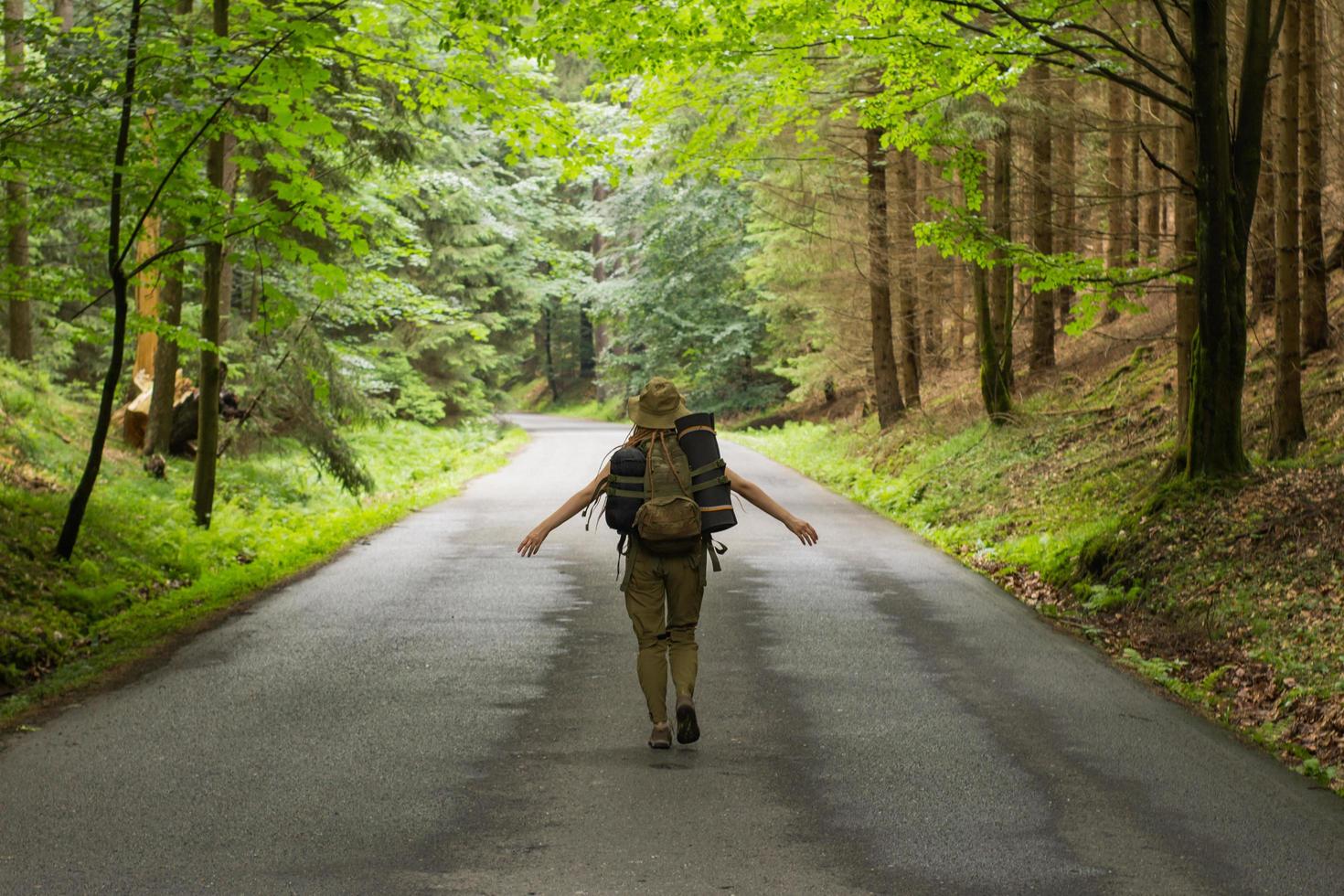 young woman hiker walking on narrow road through summer green forest photo