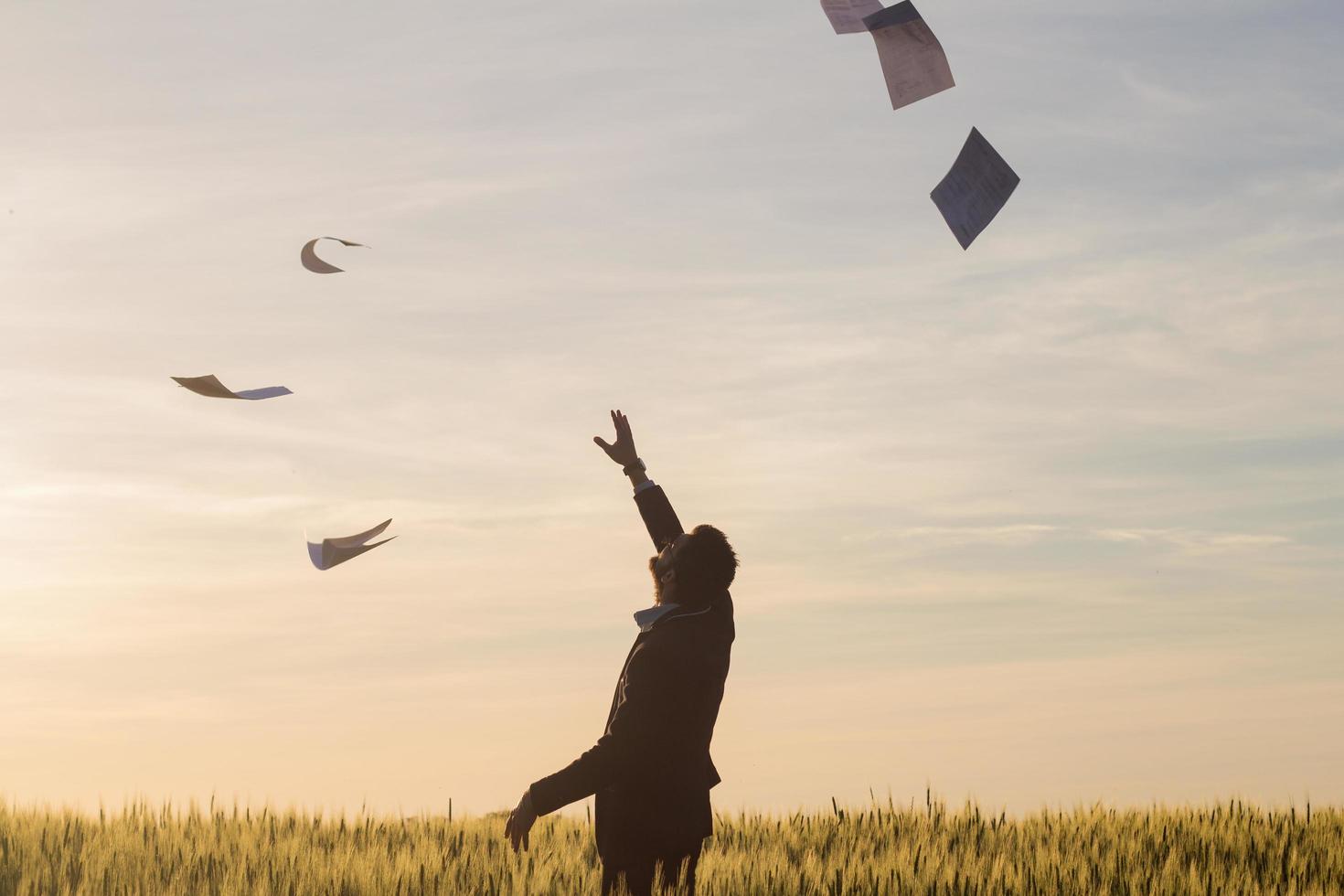 retrato de un joven hombre de negocios lanzando hojas de papel al aire, puesta de sol en el fondo de los campos de verano foto