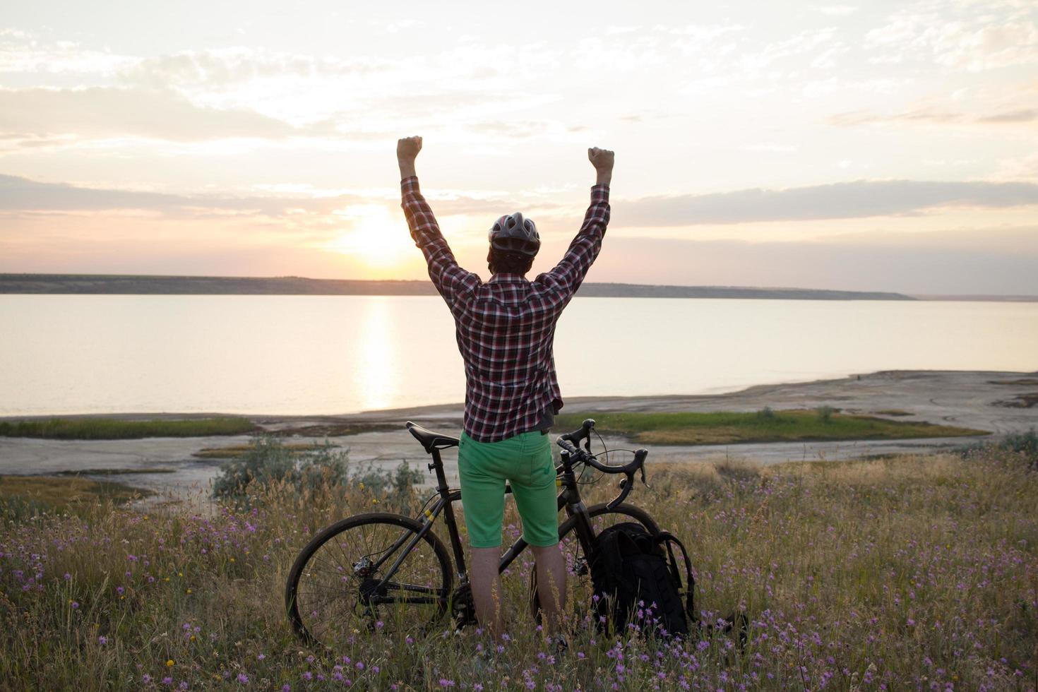 silueta de un hombre con bicicleta de carretera de gira mirando y haciendo una foto de la puesta de sol en el lago en el teléfono celular