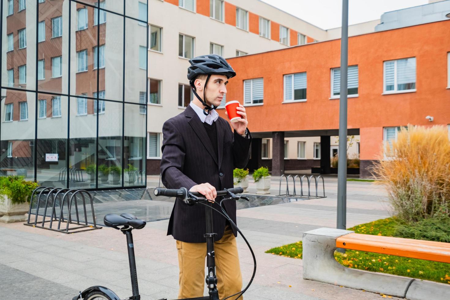 Young male businessman with bicycle and cup of coffee or tea walking outdoors photo