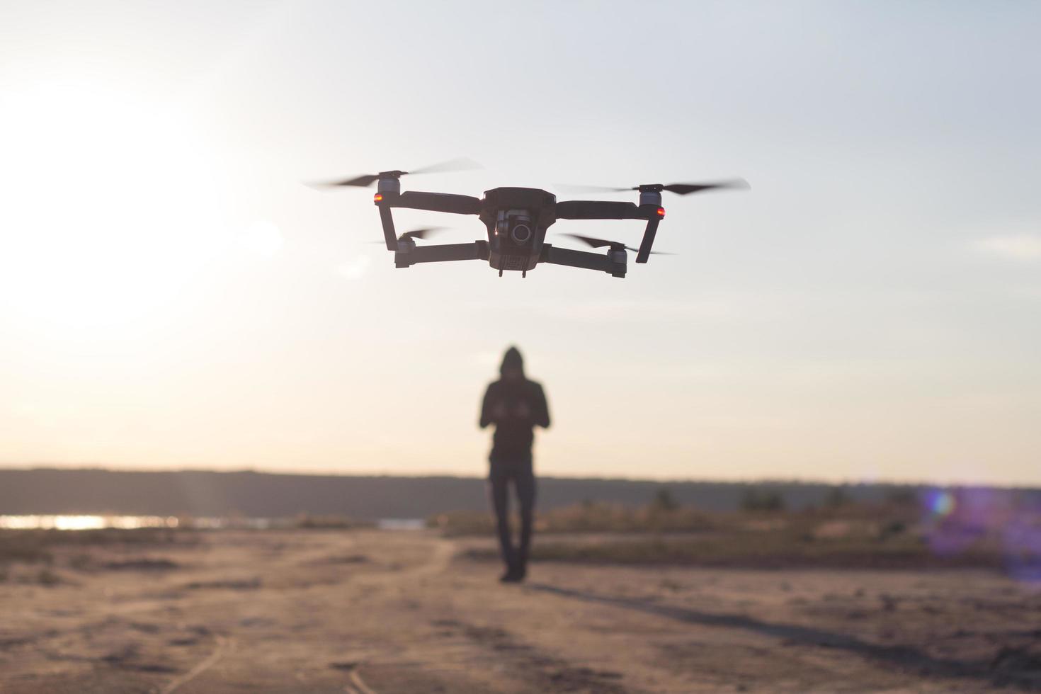 picture of black flaying quadrocopter dron and pilot siluette in sunset light background, tourist use dron helicopter to photography or filming desert landscapes photo